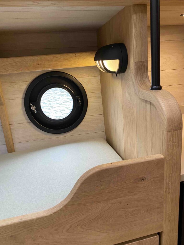 Een slaapplaats naast de patrijspoort, met uitzicht op het water vlak naast het bed.